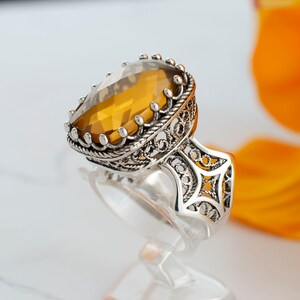 May include: A silver ring with an intricate filigree design and a large, oval-shaped amber gemstone.