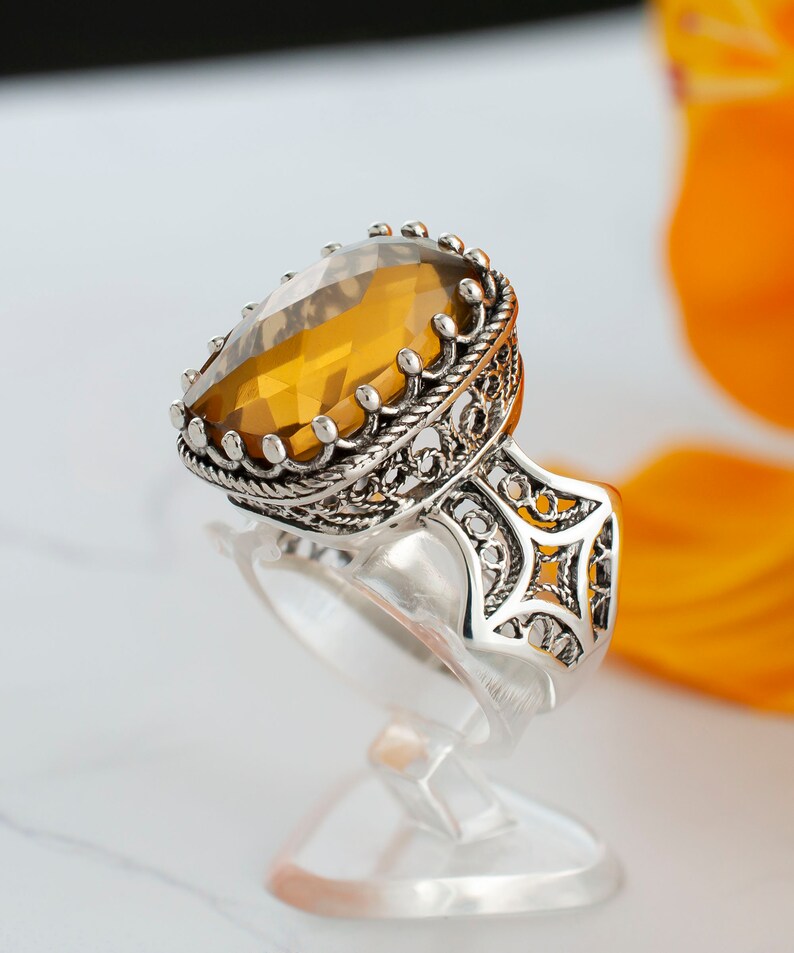 May include: A silver ring with an intricate filigree design and a large, oval-shaped amber gemstone.