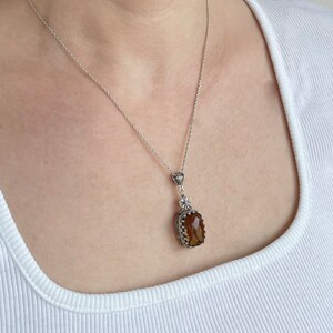 May include: A silver chain necklace with a brown gemstone pendant. The pendant is set in a silver frame with intricate details.