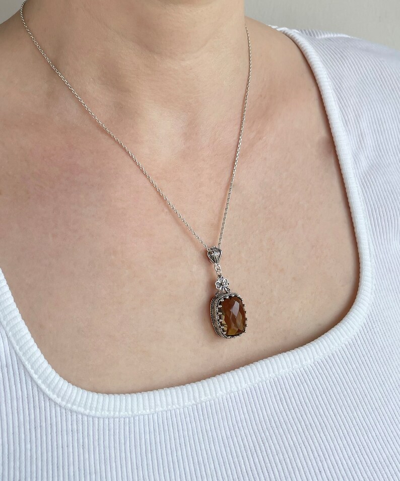 May include: A silver chain necklace with a brown gemstone pendant. The pendant is set in a silver frame with intricate details.