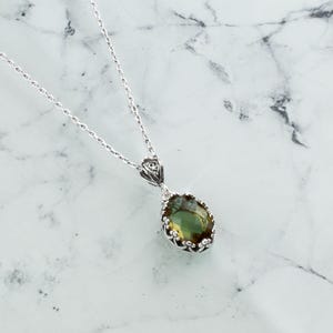 May include: A silver chain necklace with a green gemstone pendant. The pendant is oval shaped and has a detailed silver frame.