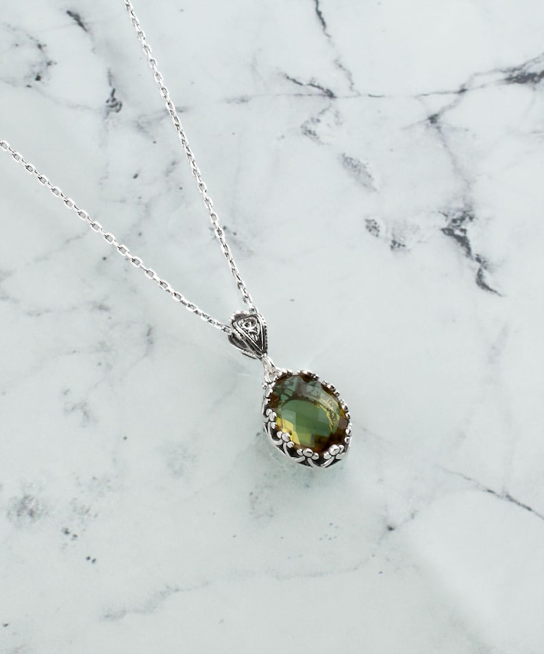 May include: A silver chain necklace with a green gemstone pendant. The pendant is oval shaped and has a detailed silver frame.