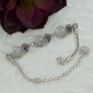 May include: A silver bracelet with three purple gemstones set in filigree circles. The bracelet has a delicate chain with a clasp and a decorative charm.