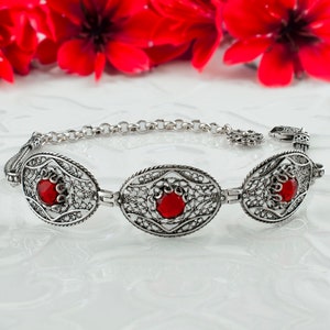 May include: A silver bracelet with three red gemstone accents. The bracelet features a delicate filigree design.