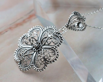 May include: A silver filigree pendant necklace with a flower design. The pendant is intricate and delicate, with a small crystal in the center.