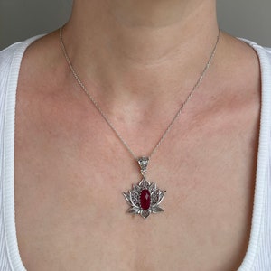 Op de afbeelding: Een zilveren ketting met een rode edelsteen hanger in de vorm van een lotusbloem.