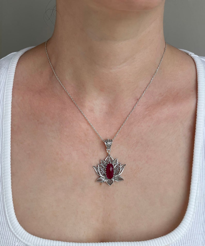 Op de afbeelding: Een zilveren ketting met een rode edelsteen hanger in de vorm van een lotusbloem.