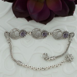 May include: A silver bracelet with three purple gemstones and a filigree design. The bracelet has a chain link closure and a decorative charm.