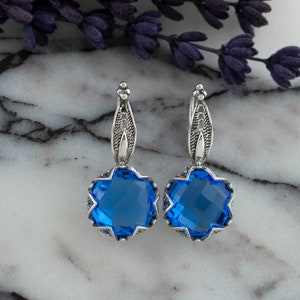 Op de afbeelding: Een paar zilveren oorbellen met blauwe edelsteen druppels. De oorbellen hebben een delicaat filigraan ontwerp en zijn perfect om elke outfit een vleugje elegantie te geven.