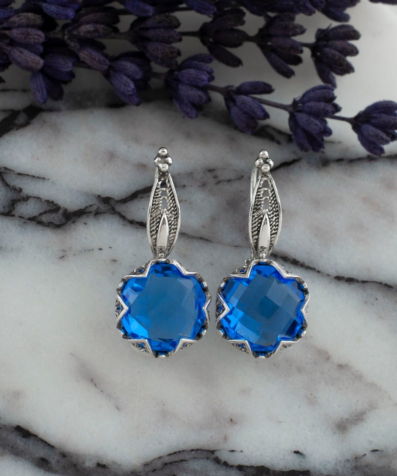 Op de afbeelding: Een paar zilveren oorbellen met blauwe edelsteen druppels. De oorbellen hebben een delicaat filigraan ontwerp en zijn perfect om elke outfit een vleugje elegantie te geven.