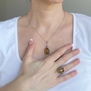 May include: A silver necklace with a brown gemstone pendant and a matching ring. The necklace and ring feature a delicate, ornate design.