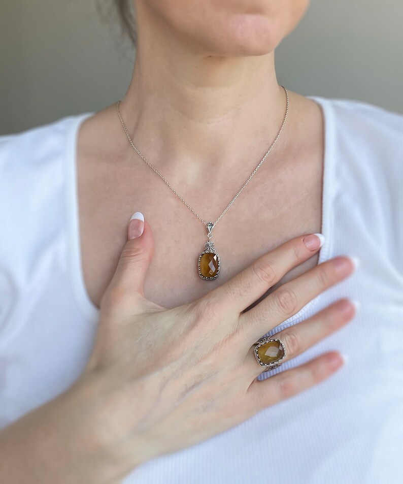 May include: A silver necklace with a brown gemstone pendant and a matching ring. The necklace and ring feature a delicate, ornate design.