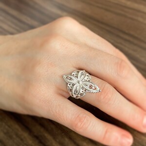 May include: A silver filigree ring with a floral design. The ring is on a person's finger.