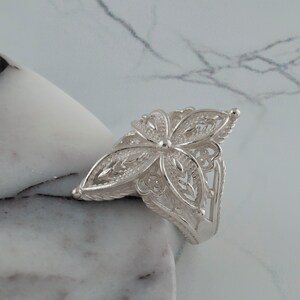 May include: A silver filigree ring with a flower design. The ring is delicate and intricate, with a floral pattern that is both elegant and feminine.