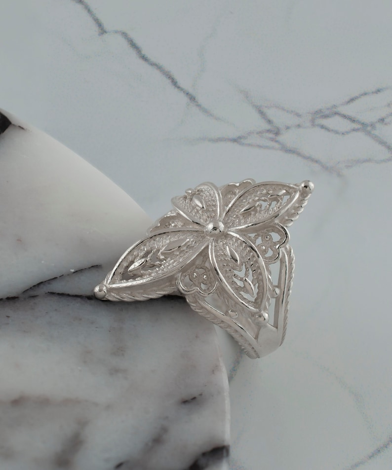 May include: A silver filigree ring with a flower design. The ring is delicate and intricate, with a floral pattern that is both elegant and feminine.