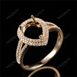 May include: A gold ring with a heart-shaped setting for a gemstone. The ring is adorned with small diamonds around the setting and band.