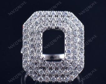 May include: A silver ring with a large, square-shaped emerald cut setting surrounded by a halo of smaller diamonds. The ring is set with a double row of diamonds around the halo.