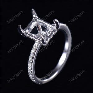 May include: A silver ring with a square-shaped setting for a gemstone. The ring has a band of small diamonds.