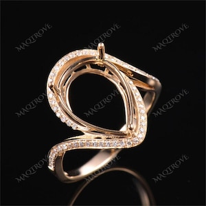 May include: A gold ring setting with an unusual, open design. The ring has a central setting for a gemstone, surrounded by a swirling, embellished band. Small, clear stones are set along the band, adding sparkle.