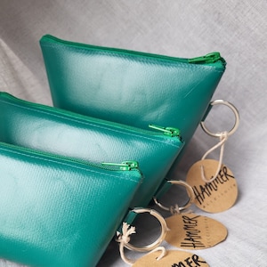 Könnte beinhalten: Drei türkisfarbene Reißverschlusstaschen mit braunen Etiketten, auf denen "Hammer Accessories" steht.