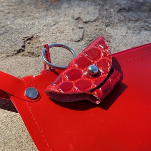 Könnte beinhalten: Ein roter Leder-Schlüsselanhänger mit einem silbernen Ring und einem kleinen roten Lederbeutel. Der Beutel hat einen silbernen Druckknopfverschluss.