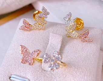 Puede incluir: Un conjunto de pendientes de mariposa y un anillo con diseño de mariposa. Los pendientes son de oro y tienen piedras transparentes, mientras que el anillo es de plata y tiene piedras transparentes.
