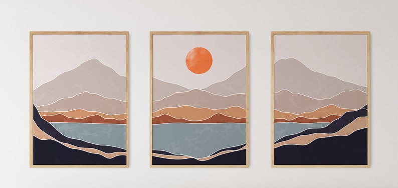 May include: A set of three abstract landscape prints featuring a mountain range, a lake, and a large orange sun. The prints are framed in natural wood.
