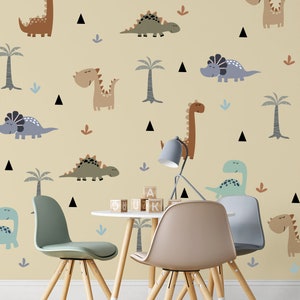 May include: A light yellow wall with a dinosaur theme. The wall is decorated with various dinosaurs in different colors and poses. There are also palm trees and small triangles. Two wooden chairs and a table with wooden blocks are in front of the wall.