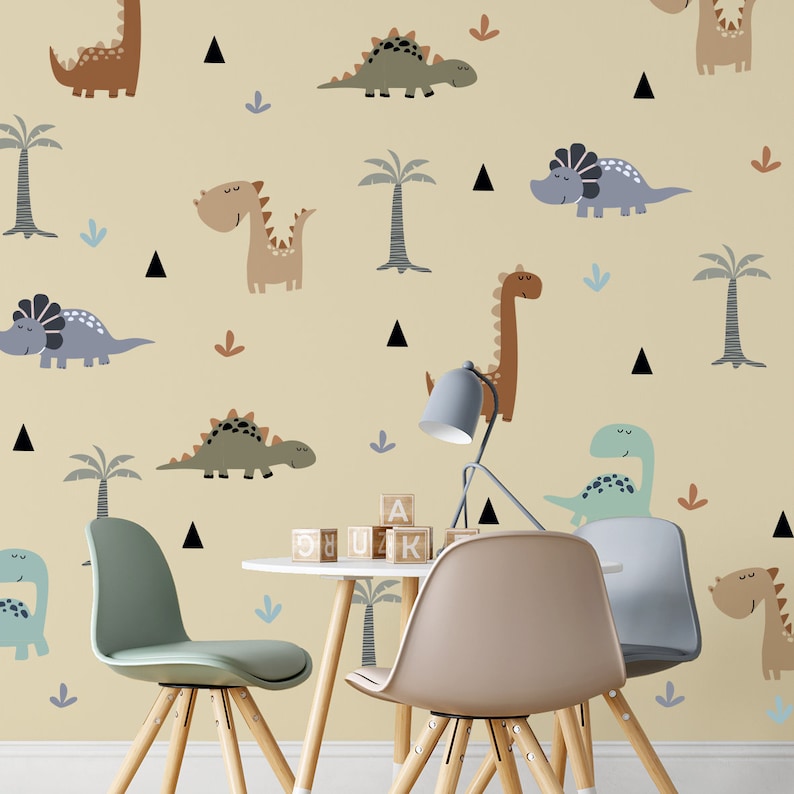 May include: A light yellow wall with a dinosaur theme. The wall is decorated with various dinosaurs in different colors and poses. There are also palm trees and small triangles. Two wooden chairs and a table with wooden blocks are in front of the wall.