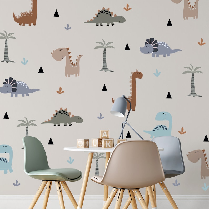 May include: A light beige wall with a dinosaur theme. The wall is decorated with various dinosaurs in different colors and patterns, including brown, green, blue, and gray. There are also small black triangles and palm trees on the wall. Two wooden chairs and a white table with wooden legs are in front of the wall. The table has wooden blocks with letters on them.