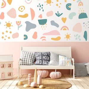Peut inclure: Un banc blanc avec des coussins, une maison de poupée et des objets décoratifs est placé devant un mur orné de formes abstraites colorées. Les coussins comprennent un motif à carreaux et un coussin avec le texte "LOVE YOU TO THE MOON AND BACK".
