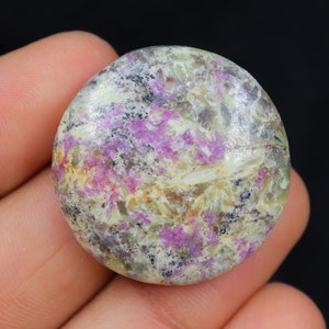 Peut inclure: Une pierre précieuse ronde, plate et en cabochon avec un motif moucheté blanc, gris et rose.