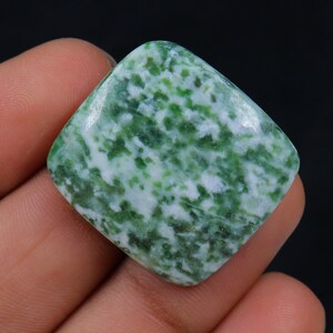 May include: A green and white cabochon gemstone with a square shape. The stone has a mottled pattern of green and white.