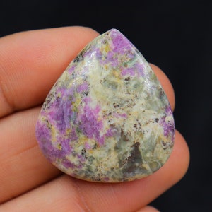 Peut inclure: Un cabochon en forme de larme de pierre précieuse rose et verte sur fond blanc. La pierre présente un motif marbré de rose, de vert et de blanc.