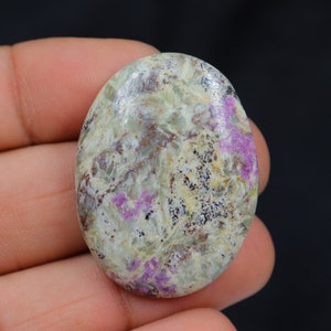 Peut inclure: Pierre précieuse en cabochon de forme ovale avec un motif marbré blanc, gris et rose. La pierre a une surface lisse et polie.