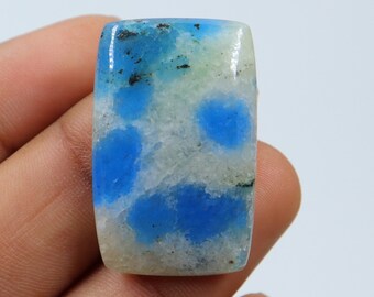 May include: A rectangular, light blue and white gemstone with a mottled pattern. The gemstone is cut and polished.