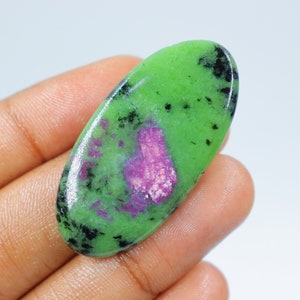 Puede incluir: Cabujón de piedra preciosa verde de forma ovalada con inclusiones negras y rosas. La piedra está engastada en un engaste de plata.