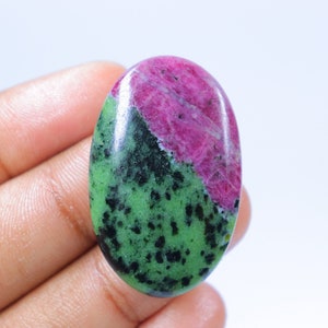 Puede incluir: Piedra preciosa ovalada de color verde y rosa con motas negras. La piedra preciosa es lisa y pulida.