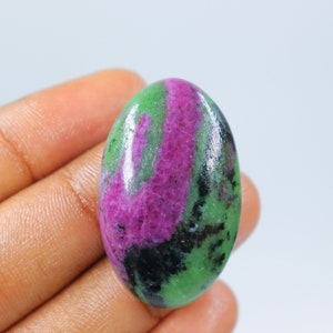 Puede incluir: Cabujón ovalado de piedra preciosa verde, rosa y negra. La piedra preciosa tiene una superficie lisa y pulida.