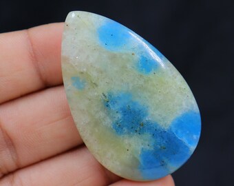 May include: A teardrop-shaped cabochon gemstone with a white base and blue and green inclusions. The stone is polished and has a smooth surface.
