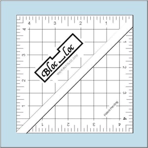 May include: A clear quilting ruler with black grid lines and measurements in inches. The ruler has a diagonal line and the text "Bloc-Loc" with the website address. The words "Patent Pending" are also visible.