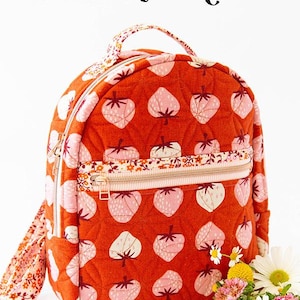 May include: A quilted orange backpack with a strawberry pattern and a floral zipper. The text "THE VIOLET BACKPACK" is at the top. The backpack has a top handle and adjustable straps. The brand "KNOT + THREAD design" is at the bottom.