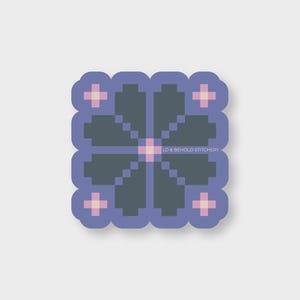 May include: A square sticker with a pixelated floral design. The flower is dark gray with a pink center and pink accents. The sticker has a light purple border and the text "LO & BEHOLD STITCHERY".