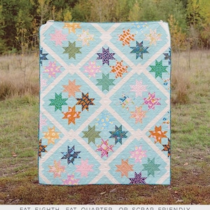 May include: A light blue quilt with a star pattern in various colors, including pink, orange, green, and blue. The quilt is titled "The Remy Quilt" and is designed by Erica Jackman. The quilt is available in baby, lap, twin, queen, and king sizes.