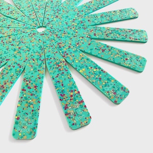 May include: A turquoise-colored, starburst-shaped quilting tool with a confetti-like pattern of red, gold, and yellow dots. Each of the 16 radiating arms has the text "Quilt with Kate" printed on it.