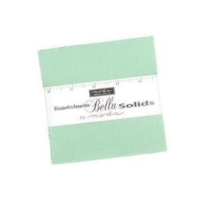 May include: A stack of square fabric pieces in a light green color, wrapped with a white band featuring the text "Bella Solids" and "Elizabeth's Favorites by moda". The fabric squares are neatly stacked and ready for quilting or crafting projects.