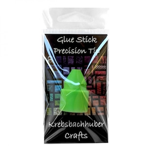 May include: A green precision tip glue stick in a clear plastic package. The package has the words "Glue Stick Precision Tip" and "Krebsbachhuber Crafts" printed on it. The background of the package has a colorful patchwork design.