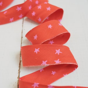 May include: A vibrant red ribbon with a repeating pattern of pink stars. The ribbon is unrolled and curled, showcasing its design. Ideal for crafting, gift wrapping, or decorative purposes.
