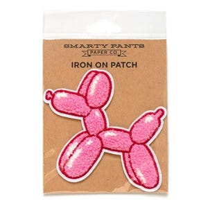May include: Pink iron-on patch of a balloon animal dog. The patch is packaged on a brown card with the text "SMARTY PANTS PAPER CO. IRON ON PATCH".