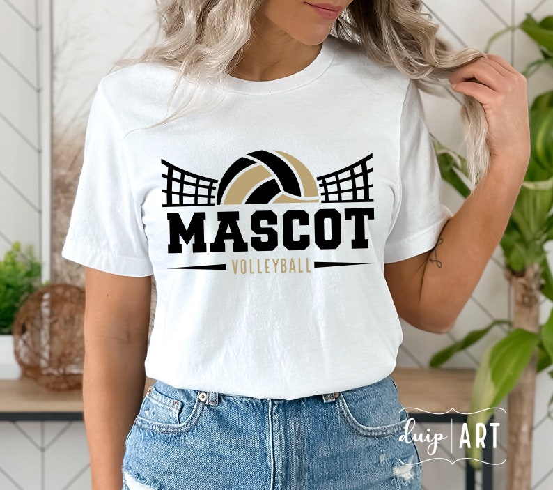 May include: White t-shirt with a black and gold volleyball graphic. The graphic features a volleyball with a net behind it. The text "MASCOT VOLLEYBALL" is below the graphic.